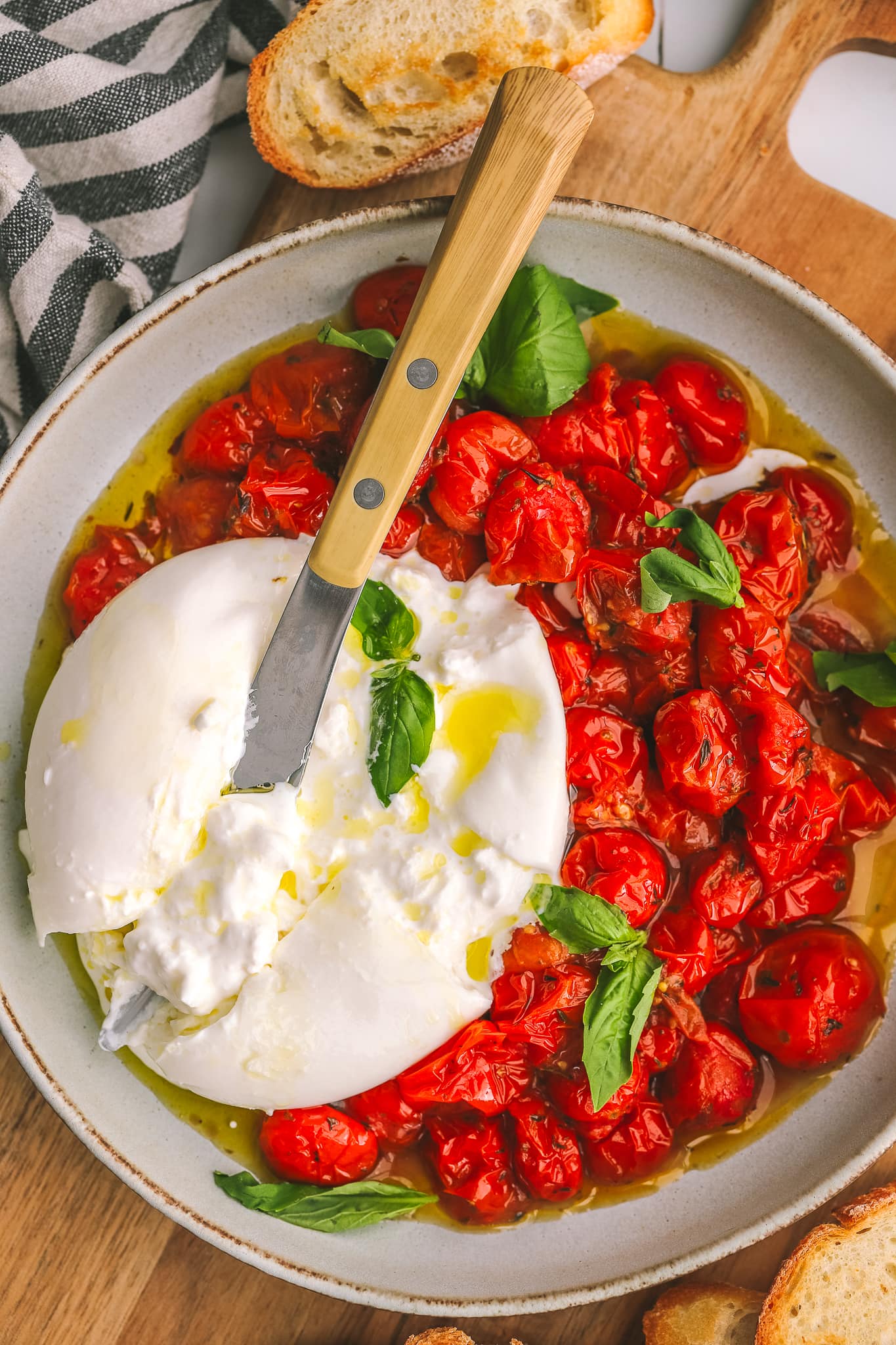 roasted tomatoes in a bowl with burrata cheese and toasted bread