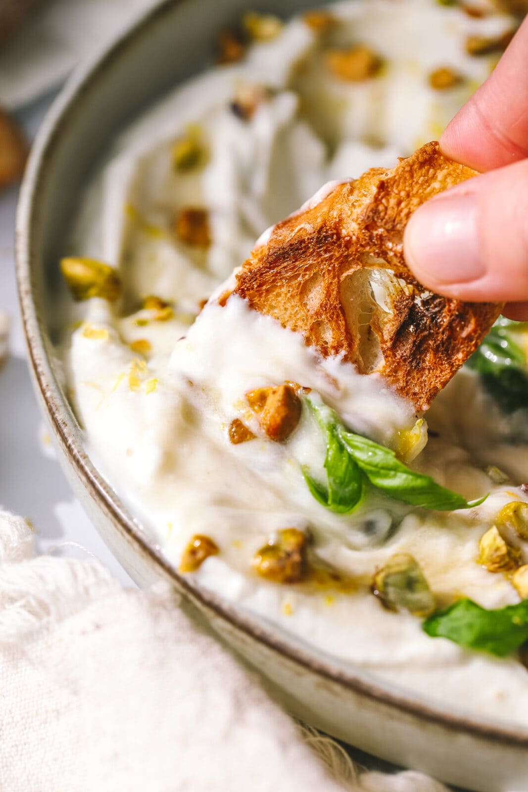 hand dipping a piece of bread into whipped ricotta