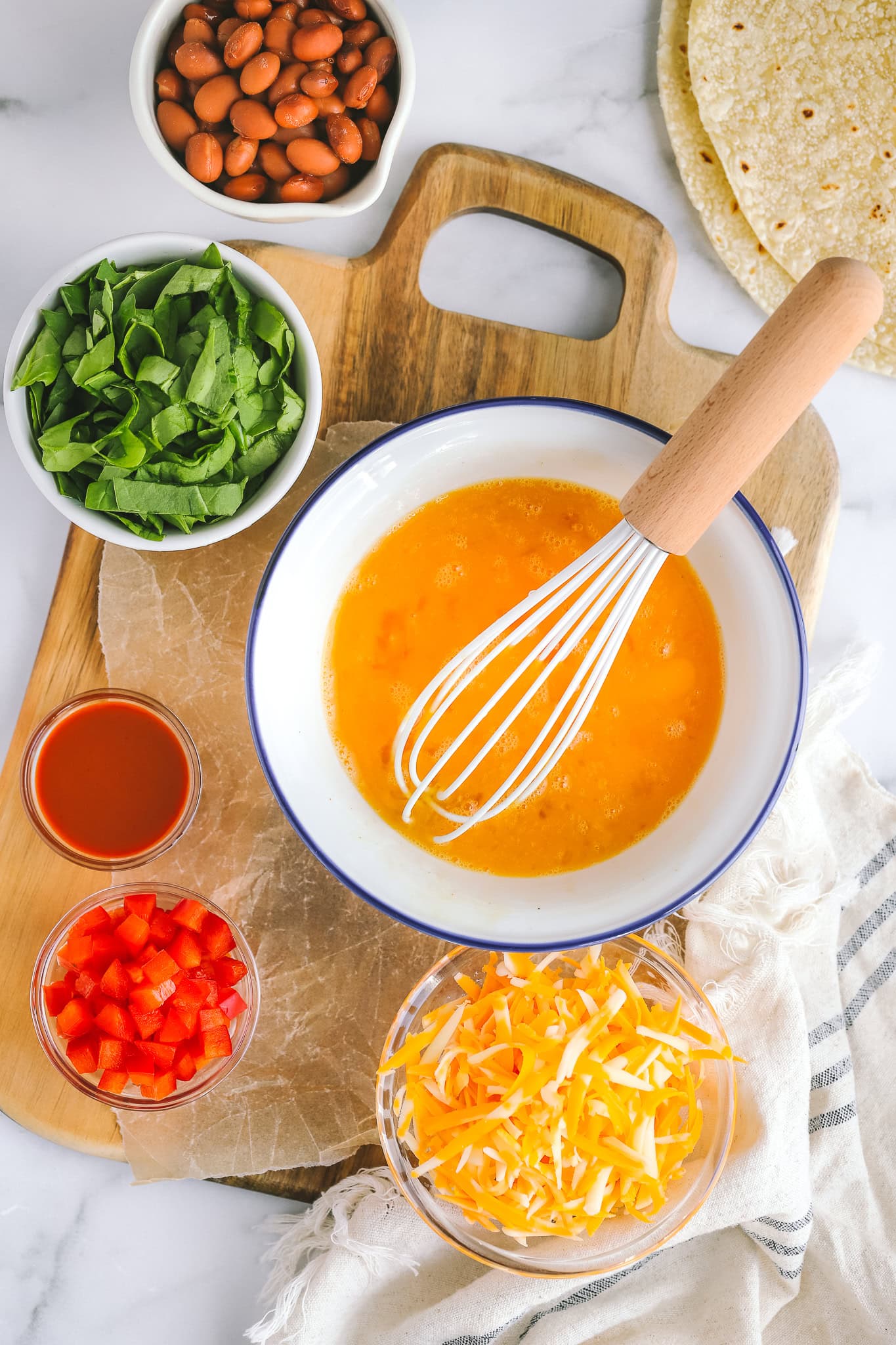 whisked eggs in a bowl, tomatoes in a bowl, spinach in a bowl, cheese in a bowl