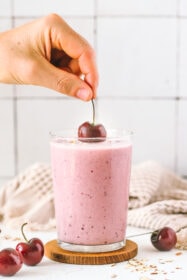 hand placing a cherry on top of the smoothie