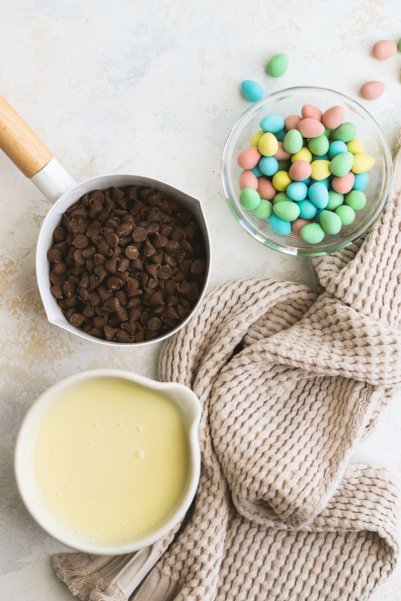 chocolate chips in a pot, sweetened condensed milk in a bowl, mini eggs in a bowl