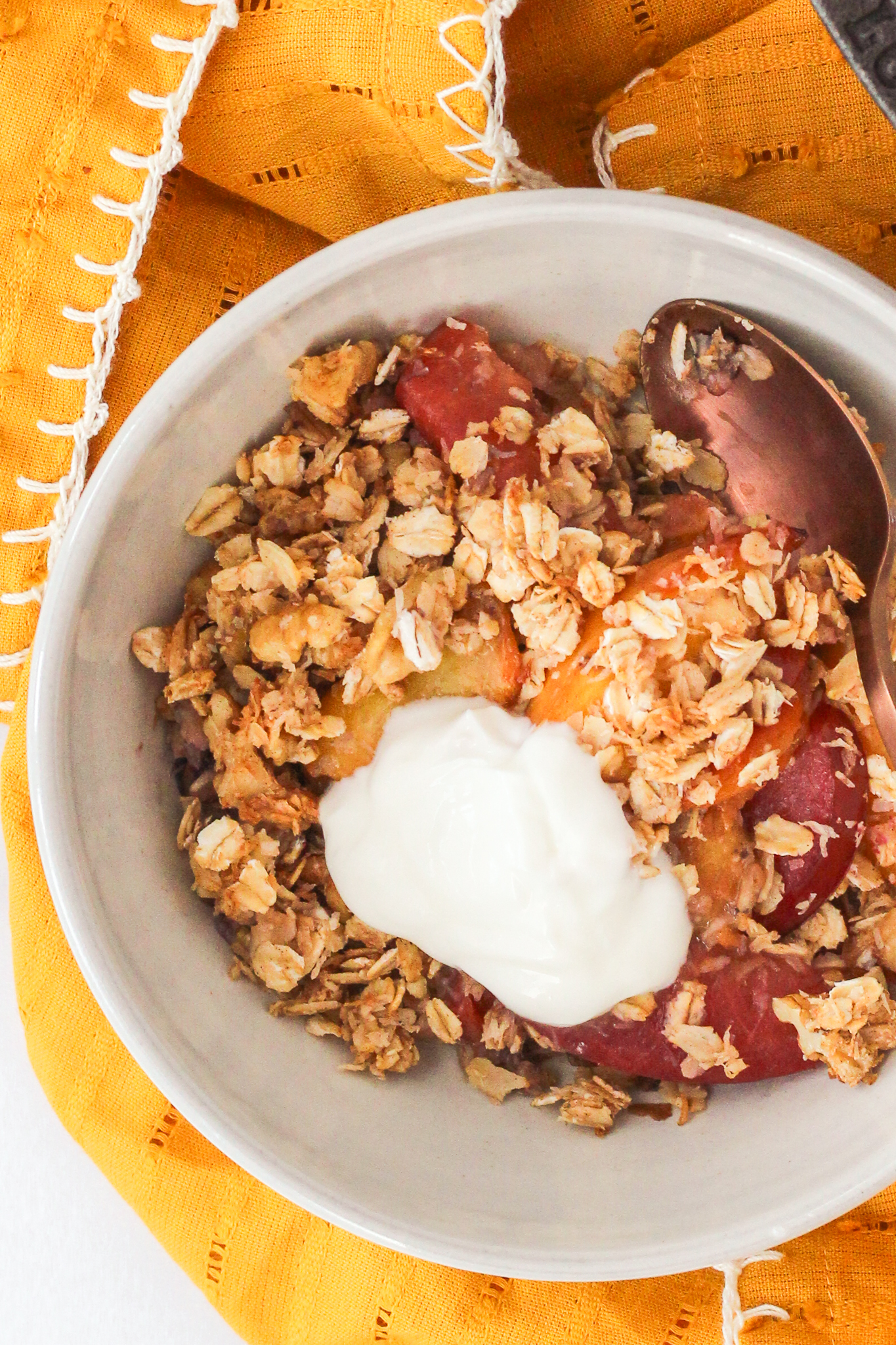 stone fruit breakfast crumble in a bowl topped with yogurt