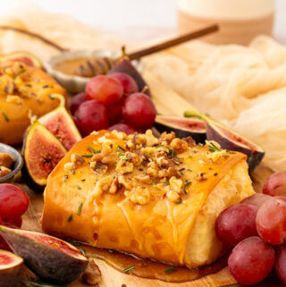 side angle of baked feta on a serving board with grapes and figs
