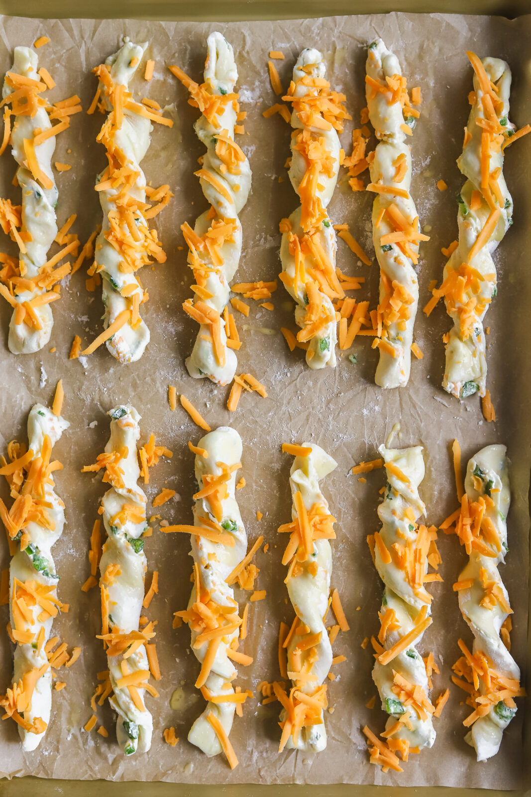 jalapeno popper cheese twists on a baking sheet with shredded cheddar cheese